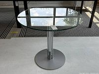 Full view of round glass top table with chrome pedestal and metal base