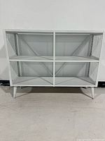 Front view of white painted credenza shelf showing four open cubbies and tapered legs