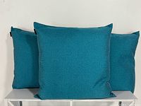 Three teal square pillows displayed to show size and color