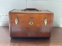 Front view of brown Samsonite train case showing latches, lock and surface wear