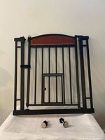 Full view of gate standing upright showing bars, arched wood accent, pet door, two mounting bolts in front