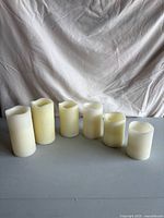 Front view of six off-white flameless pillar candles