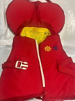 Front of red nylon child life jacket unzipped showing yellow interior label, zipper and waist buckle