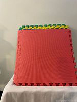 Stack of colored interlocking foam tiles showing red fronts and green, yellow, blue edges