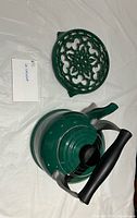 Top view of green whistling kettle with black handle and matching green cast-iron trivet
