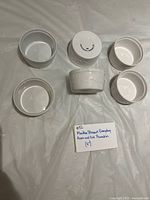 Six white stoneware ramekins, some upright showing interiors, some inverted to display embossed Acorn & Oak pattern and base mark.