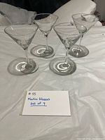 Four clear martini glasses arranged upright on white surface, identification card visible