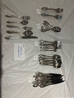 All silver-plated flatware stacks grouped by type on table; reference note showing Oneida marking visible