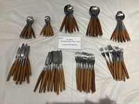 All 108 pieces of teak-handle stainless steel flatware arranged by type