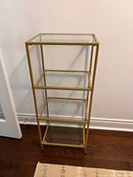 Full view of gold metal frame shelving unit with glass shelves