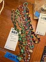 Five glass beaded necklaces laid out on wooden surface with lot tag visible
