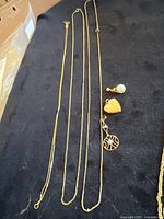 Overview of three gold chains and three pendants on dark cloth
