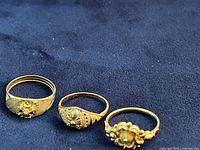 Three 22K yellow gold rings side by side on dark cloth