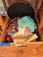cardboard box containing open hatbox filled with folded scarves, MaxSold lot tag visible