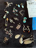 All 15 earring pairs and pin laid out on black cloth with lot note