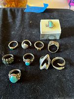 Ten sterling silver rings displayed on black cloth with ring box
