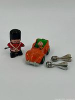 Group shot of all four toys: wind-up guard, orange car with driver, two miniature spoons