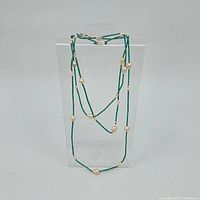 Necklace displayed vertically on clear stand showing overall length and alternating turquoise beads with pearls