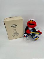 Front view of Elmo plush seated beside box