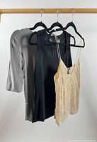 Three tops on hangers: grey 3/4 sleeve, black sleeveless, beige beaded camisole front view