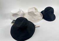 Group shot of four hats: white mesh, beige brim, black bucket, black beanie