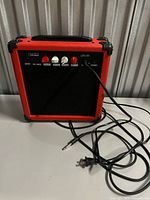 Front view of red and black AGL-20 guitar amplifier with attached power cord