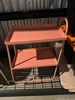 Overall view of pink metal two-tier cart on shelving unit