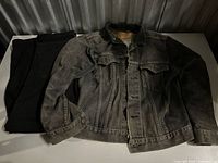 Levi's faded grey denim jacket beside folded black jeans on table
