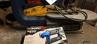 Ryobi scroll saw with yellow vehicle jack arm visible, RotoZip boxed tool in foreground