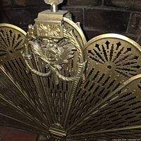 Front view of brass peacock fan screen showing pierced blades and ornate crest