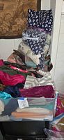 Stack of assorted folded fabrics in various colours and patterns atop storage bin