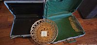 Open Samsonite briefcase left, open green suitcase right, wicker basket platter in foreground