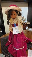 Front view of 18" Uneda doll wearing burgundy velvet dress, cream lace trim, satin bow and matching bonnet, showing face and outfit
