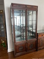 Full view of closed cabinet showing glass upper section, wood lower doors, brass handles