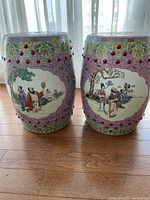 Front view of both porcelain garden stools showing painted scenes and raised studs