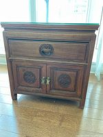 Front view showing drawer, cabinet doors, carved motifs, brass hardware, and glass top
