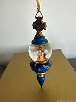 Front view of blue and gold finial ornament showing kneeling figure inside globe