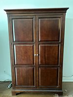 Front view of closed merlot finish TV armoire showing paneled doors and silver knobs