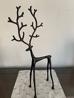 Front view of slender black metal deer sculpture on patterned base