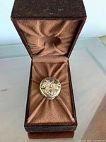 Closed pill box in presentation case showing floral relief lid