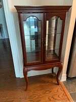Front view of solid wood glass curio cabinet showing double doors, two glass shelves, mirrored back, cabriole legs