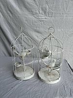 two white metal birdcage candle holders side by side