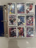 Binder open showing first sheet of nine assorted hockey cards including football cards