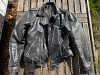 Front view of black leather motorcycle jacket laid flat on wooden surface