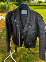 Front view of black leather biker jacket on hanger showing overall design