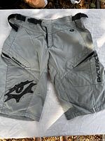 Front view of gray Race Face mountain bike shorts showing logos, zipper fly and thigh pockets
