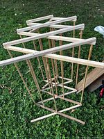 Full view of folding wooden clothes drying rack on grass, showing structure and wear