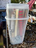 Tall clear plastic storage bin with lid containing wrapping paper rolls