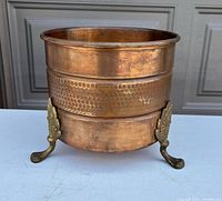 Front view of copper planter showing hammered band and two brass claw feet