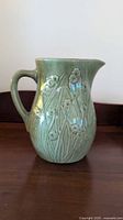 Front view of green glazed stoneware pitcher showing Art Nouveau floral relief